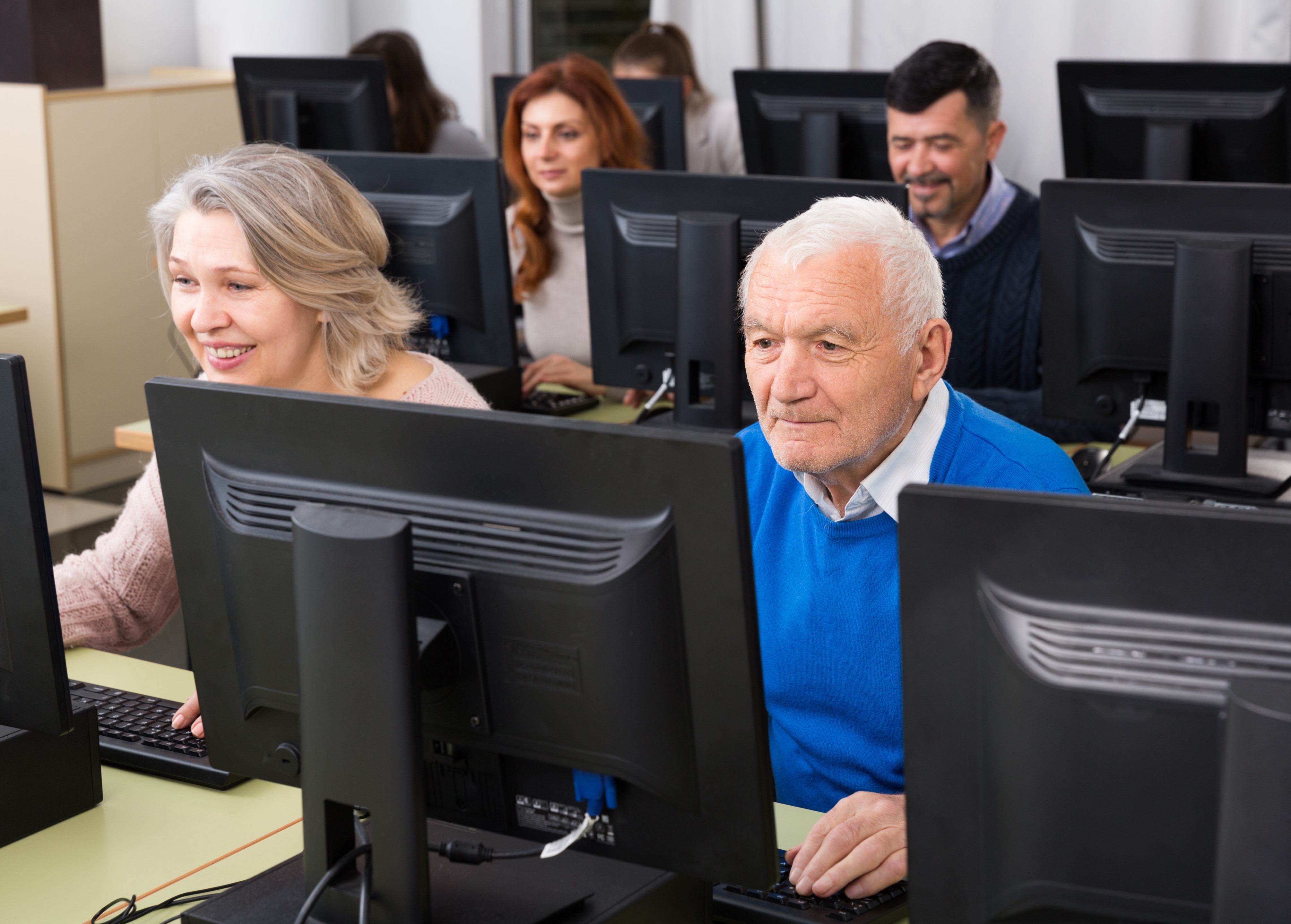 Photo of several elderly people behind computer screens smiling at the screens